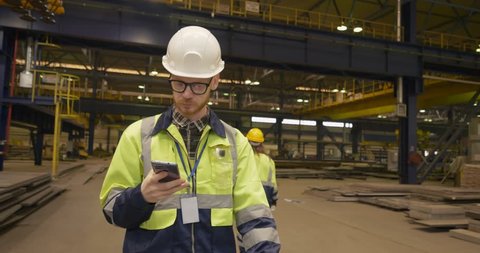 Male factory worker talks by cellular phone at a big plant
