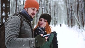 Close up portrait. Couple watching videos in a smart phone on winter holidays with the snowy forest in the background. use smartphone, copy space. social networks, laughs and rejoices, smile on face