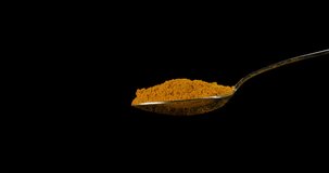 Spoon and Curry Powder falling against Black Background, Slow motion 4K