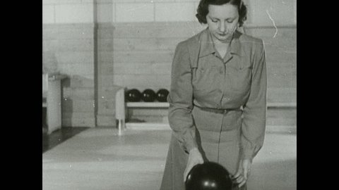 1930s: Woman picks up bowling ball, stands at front of lanes, looks down lane, bowls a strike. Woman holds ball, looks at lane, shuffles forward, falls down.