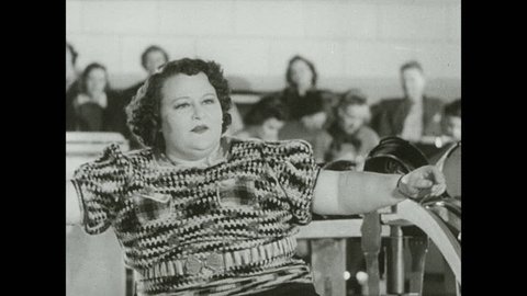 1930s: Woman sits at front of bowling lane, looks defeated, gets hit in head with ball, falls over. Girl in audience covers her eyes, peeks through. Woman prepares to bowl.