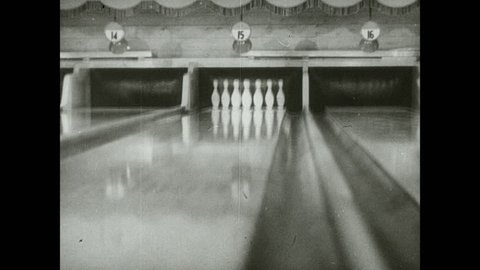1930s: Bowling ball travels down lane, knocks down all pins. Woman stands at top of lanes.