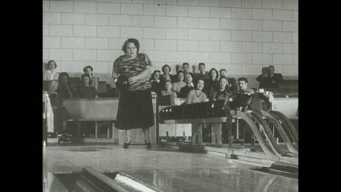 1930s: Woman looks down lane, swings bowling ball back and forth, shuffles down lane, stops, gently rolls ball down lane.