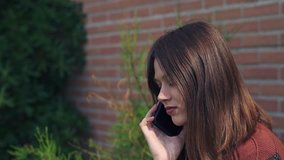 Beautiful young Woman talking to the phone,outdoors, brick wall background, Slow motion clip with gimbal
