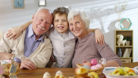 Portrait of adorable little boy and his grandparents embracing each other and smiling at camera at Easter