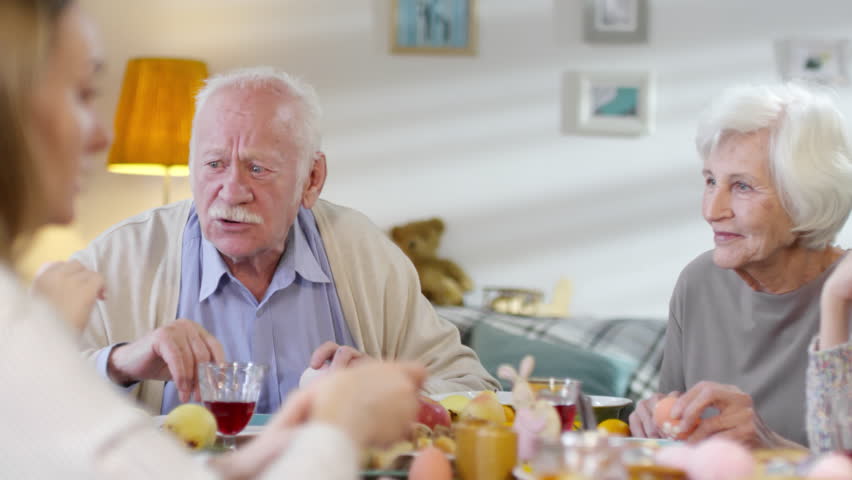 Medium shot of loving grandparents talking to grandchild while family having Easter dinner together
