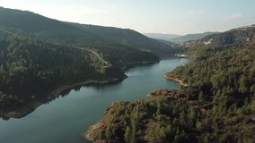 Video from the air. Video camera  circling over the Troodos mountains and over the lake in Cyprus. Coniferous forest, hills and winding shore , the meadows on the background of blue sky