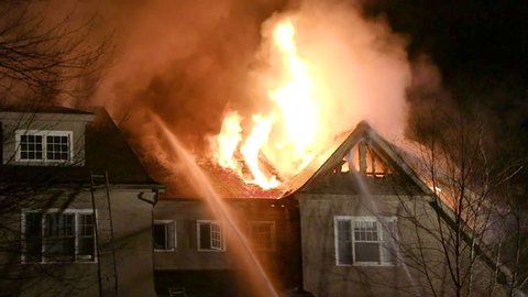 Flames Shoot out from the Roof of a Large House as Fire Hoses Fight the Blaze, Close Up Shot