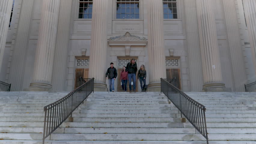 Four attractive young college students talking, laughing, and walking down steps from a library at a large public University - slow motion