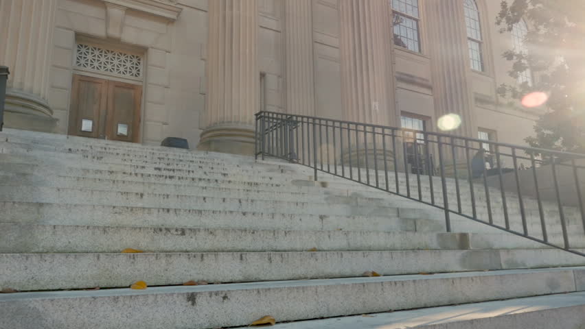 Two men and two women college friends walking up stairs towards a university library in slow motion with lens flare