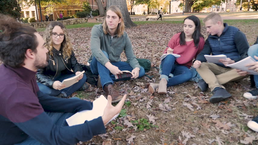 Male college student leading a discussion while sitting outside with his classmates on a university campus in slow motion