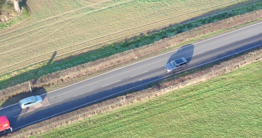 Aerial tracking shot of a SUV 4X4 vehicle driving along a country road into a village.