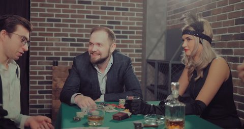 Wealthy men talk and play at the game table with beautiful women. On a green table are gaming chips, cigarettes, money and alcohol.