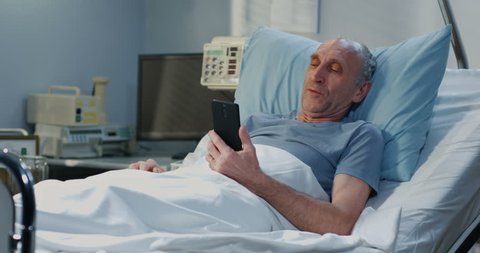 Medium shot of senior adult patient using video call in hospital room