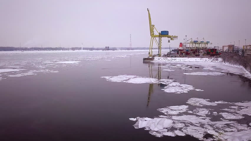 Cinematic drone / aerial footage ascending over the lake showing a port, a ship, containers, the city of Montreal, Quebec, Canada on the background during winter season.