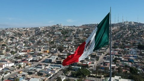 Sweeping aerial shot of the Mexican flag waving over Tijuana.