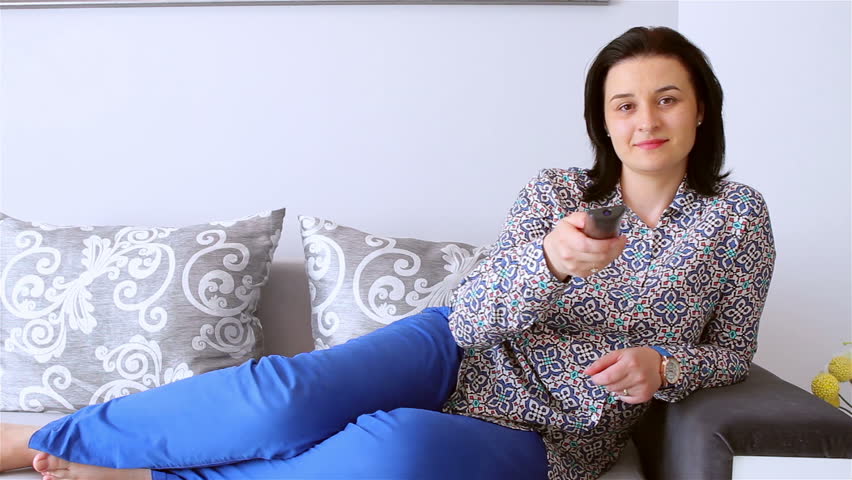 Young woman with remote control watching television in living room