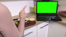 Woman making burger in kitchen near laptop with green screen
