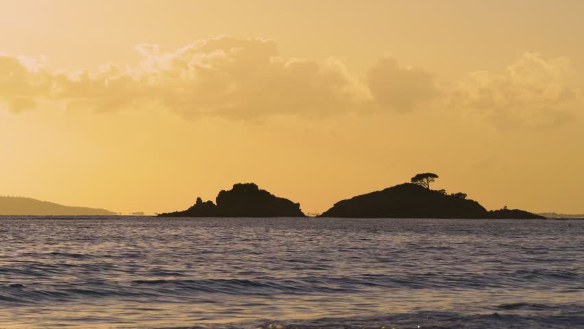 Slow pan on two small silhouette island at golden sunset