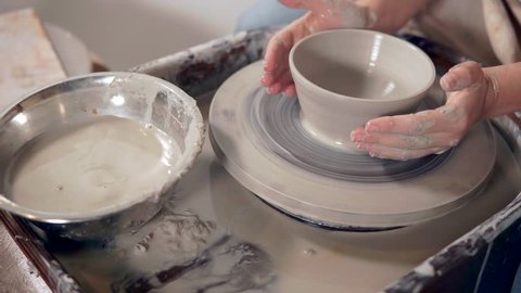 Detail view of process of modeling ceramic tableware using potter's wheel. Woman is touching clay blank and making shape of bowl, close-up