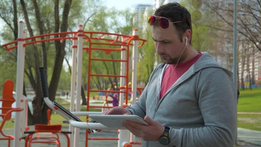 Man stands near sports ground and holds in hands tablet pc. Sportsman uses tablet computer at sport ground