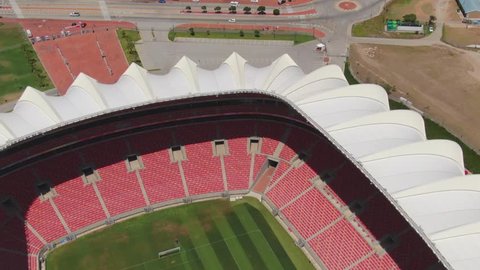 Port Elizabeth, South Africa - circa 2010s: Close view of Nelson Mandela Bay Stadium seats and green grass pitch with lawnmower. Aerial pull back and tilt up to reveal some traffic on nearby roads