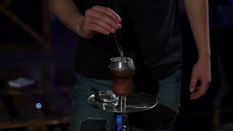 Close-up of a man changes a burnt coal in a hookah in a dark hookah bar. Slow motion. Smoking Concept. Traditional Asian relaxation.