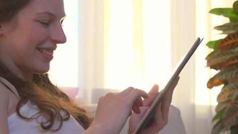 Beauty young woman using PC Tablet. Female at home sitting on the sofa and chatting. Tablet computer. Slow motion 240 fps, full HD 1080p. 