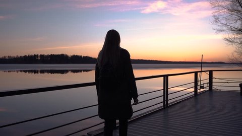 beautiful sunset, beautiful girl walking along the pier in the Harbor, and watching the sunset, the sky reflected in the water, spring ice melting on the water, vacation, out of town, camera moving, s