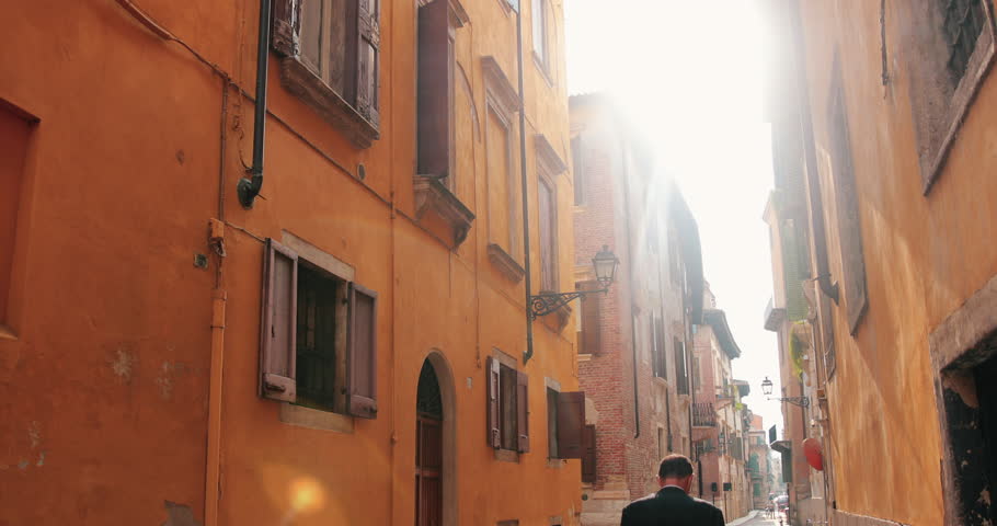 Slow motion clip of a narrow street in Verona, Italy, with a business man walking down it.