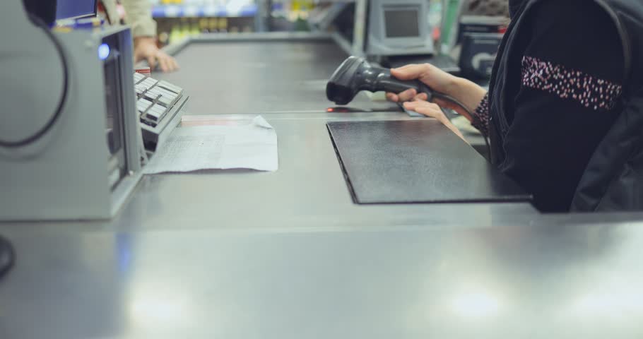 Buyer puts the goods on the cashier. Cashier punches the products by scanning. Close-up.