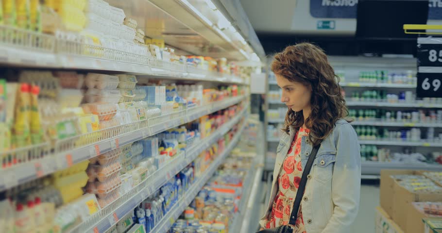 Young woman chooses eggs at the grocery store. Girl takes a cassette of eggs and puts it in the cart. Royalty-Free Stock Footage #1028002040