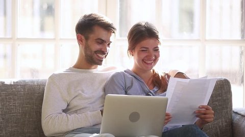 Happy positive young couple holding reading good news in document letter, smiling family checking easy service to pay paper domestic bills online on laptop discuss budget, satisfied with money refund
