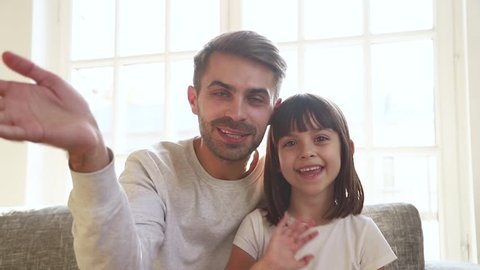 Happy cute little child girl and dad vloggers waving hands recording vlog at home, father with kid daughter looking at camera webcam make online video call  talk laugh communicating online