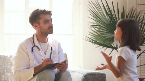 Cute little child girl talking to male doctor making notes doing medical checkup, man pediatrician holding clipboard listening to preschool kid girl telling complaint on consultation appointment