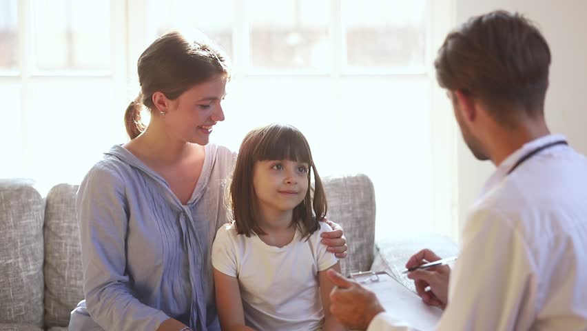 Cute funny kid girl patient sit on couch with mom talking to male doctor, small preschool child with parent visiting pediatrician doing medical checkup laughing having fun at medical consultation | Shutterstock HD Video #1028009600