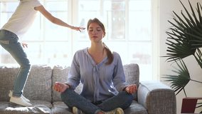 Mindful single mother meditating sitting on sofa while active energetic child daughter jumping playing, calm young mom doing yoga exercise at home for stress relief relaxing with naughty little kid - Powered by Shutterstock - Get 15% off with code: PIKWIZARD15