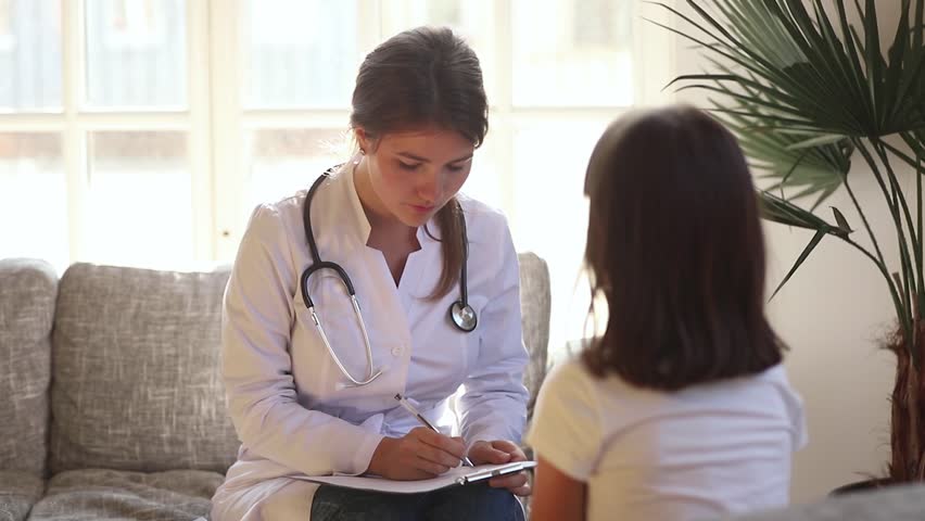 Young female pediatrician holding clipboard listening to kid girl tell complaints on checkup consultation, woman doctor make notes talking to preschool child fill patient form at medical appointment Royalty-Free Stock Footage #1028009609