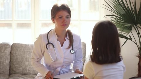 Young female pediatrician holding clipboard listening to kid girl tell complaints on checkup consultation, woman doctor make notes talking to preschool child fill patient form at medical appointment