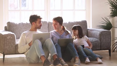 Happy modern family sit on floor in living room talking using devices, parents mom dad and child daughter having fun with laptops and phone at home, people and gadgets, technology addiction concept