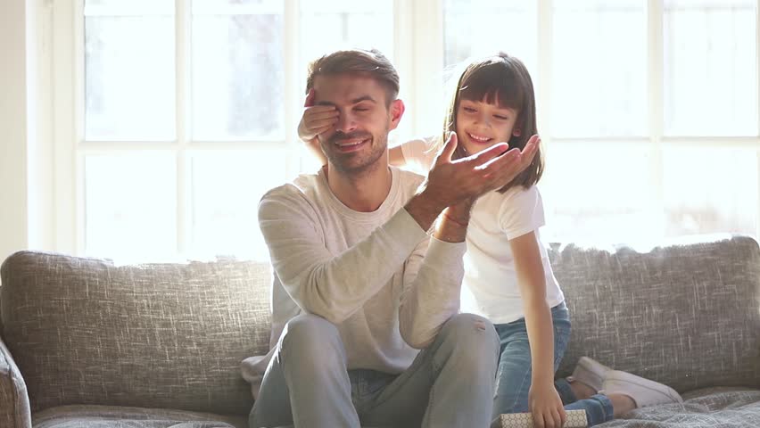 Cute kid daughter make surprise present covering eyes of happy dad receive gift box sit on sofa, little child girl congratulating parent smiling excited daddy on fathers day birthday embrace at home
 Royalty-Free Stock Footage #1028009654