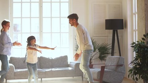 Happy cute blindfolded kid girl playing hide and seek activity catching parents mom dad in living room, little child daughter having fun laugh enjoy tag touch game with family mother father at home