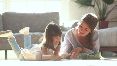 Happy family mother baby sitter teaching cute child girl playing on warm floor at home, mom helping kid daughter learning drawing coloring with pencils together enjoy creative activity in living room