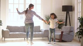 Active young mom babysiter and cute little kid daughter jumping dancing in modern house living room, happy family mother with child girl having fun enjoy playing funny activity together at home - Powered by Shutterstock - Get 15% off with code: PIKWIZARD15