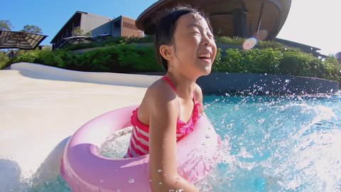 Happy little asian girl play water on waterslide of water park in summer sunny day