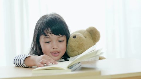 Asian kid girl reading the book with her lovely doll. education concept.