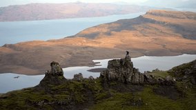 
Flying around young man climbing victoriously on top of mountain at sunset. Famous exposed rocks Old Man of Storr, north hill in the Isle of Skye island of Highlands in Scotland. 4K VIDEO 