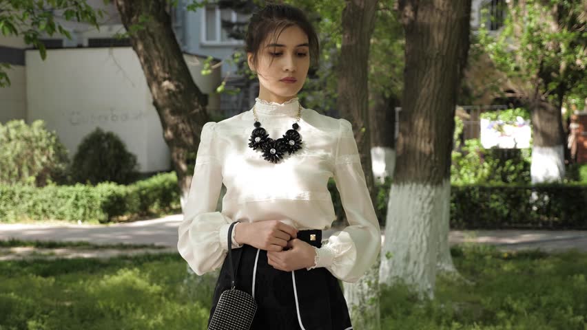 girl with hair bundle in white chiffon blouse and black skirt with big dark flower necklace and small clutch bag