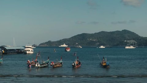 Boats floating on the seaside coast of Thailand Phuket Beach during a sunny day. Mountain in the background