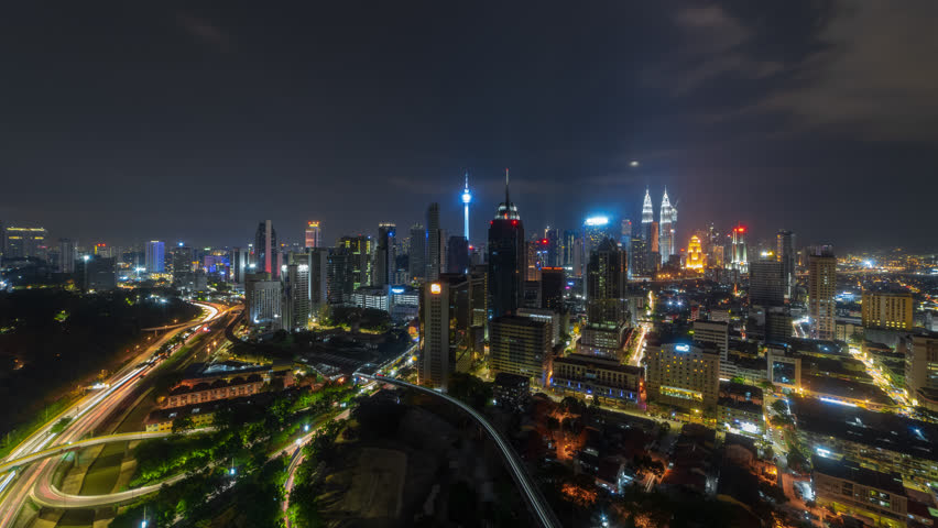 Time lapse: Night view of Kuala Lumpur city skyline with moon rising behind the city skyline and busy light trails in Malaysia.